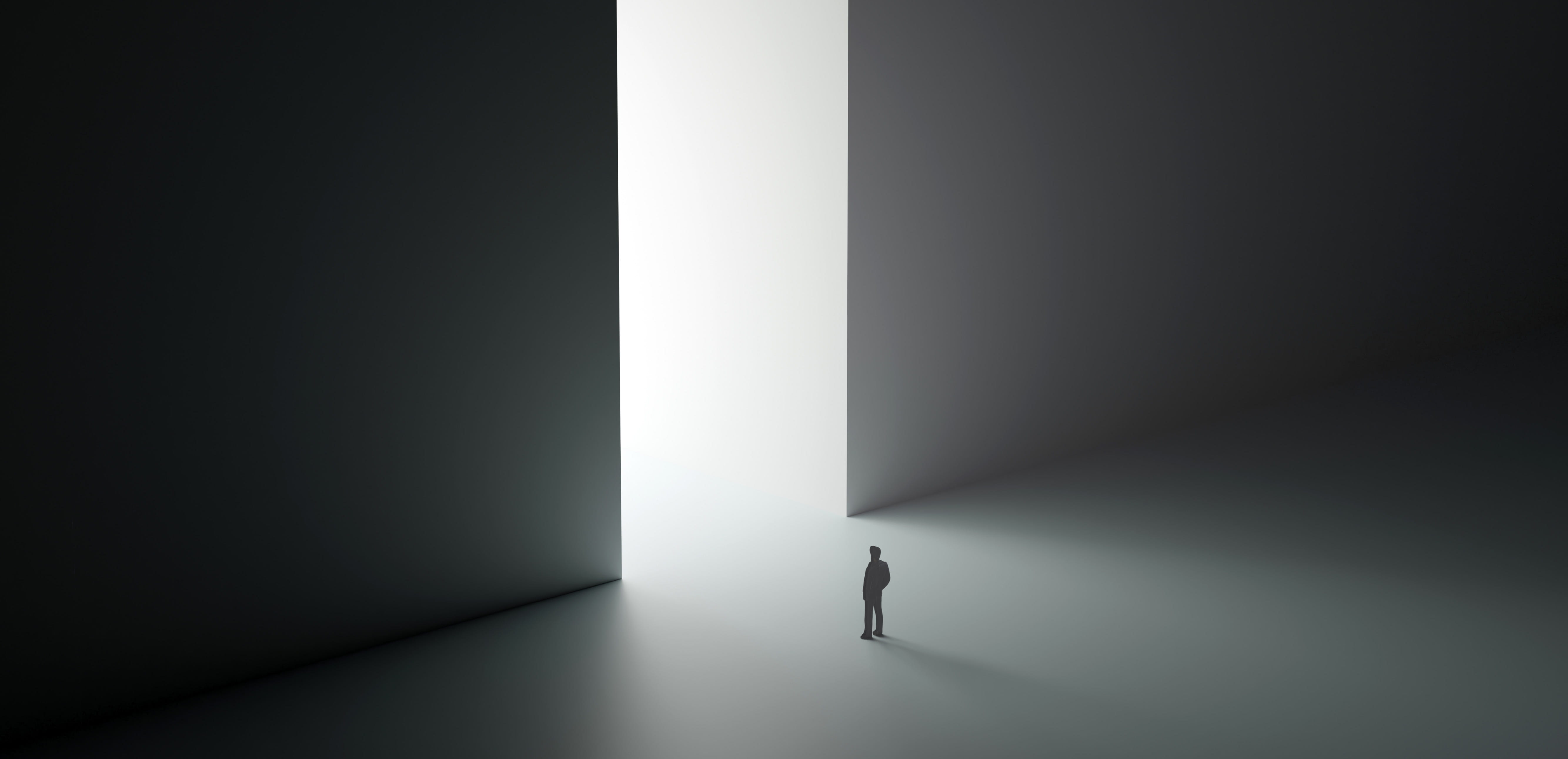 Silhouette of a person standing before a towering, bright doorway in a dark, minimalist space.
