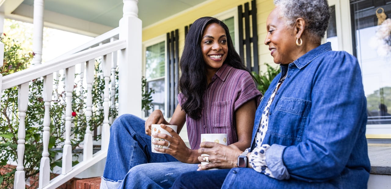 Mother and adult daughter talking on a front porch, symbolizing open conversations about passing on a family home to the next generation.
