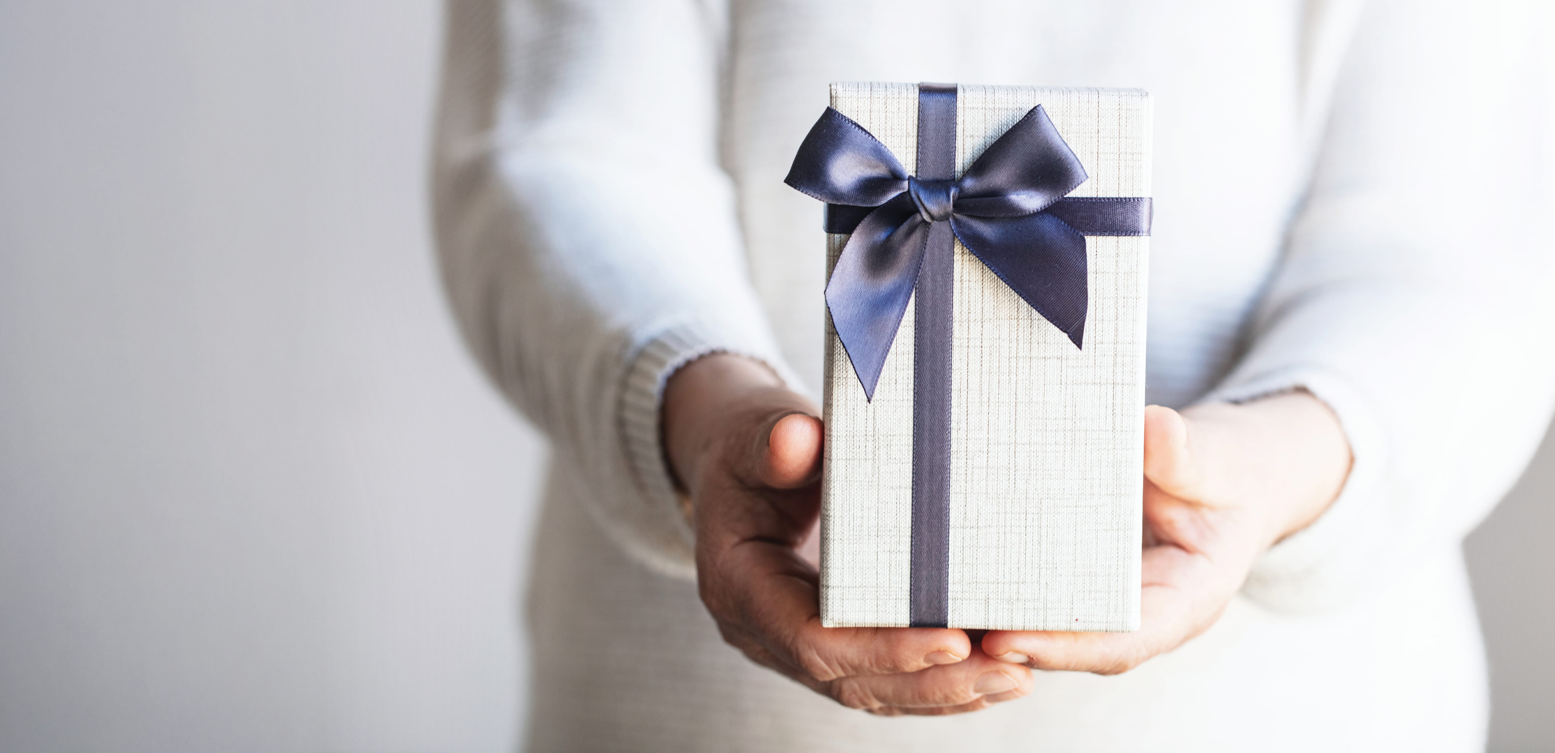 Hands offering a wrapped gift box with a navy ribbon.