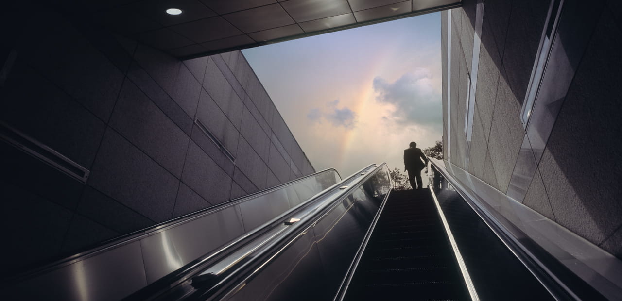 Person ascending an escalator toward daylight, symbolizing 2026 tax law changes limiting high earners’ pre-tax catch-up retirement contributions.