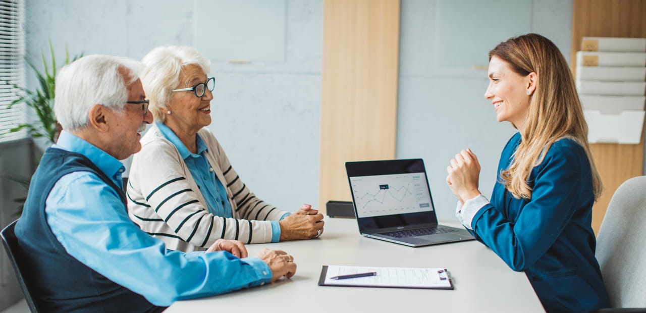 A couple sits across from their accountant at a desk reviewing documents and a laptop screen during a tax‑planning meeting.